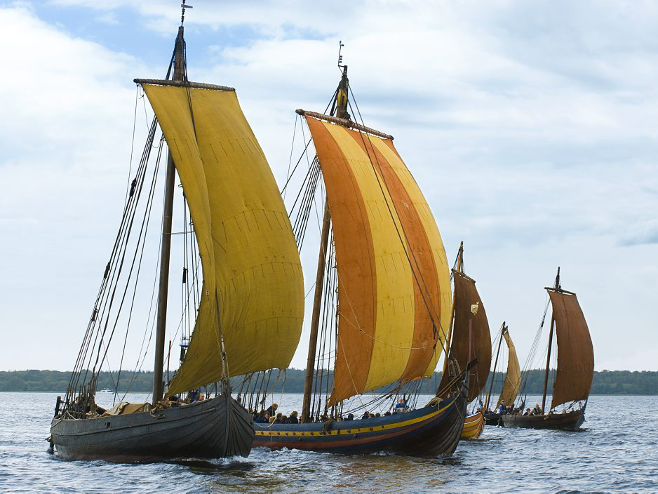 [Translate to english:] De fem Skuldelev rekonstruktioner, Ottar, Havhingsten fra Glendalough, Helge Ask, Roar Ege og Kraka Fyr sejler sammen på Roskilde Fjord. 