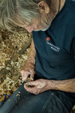 Boatbuilder Hanus Jensen carves a cork plug to fit into a knot hole. Photo: Werner Karrasch / The Viking Ship Museum in Roskilde, Denmark