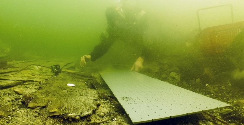 Marinarkæologen gør klar til at løfte de skrøbelige skibsdele ud af vandet på en tilpasset plade, som skibsdelen pakkes ind sammen med for at stabilisere og beskytte