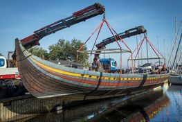 [Translate to english:] Vikingeskibsmuseets medarbejdere og de fremmødte tilskuere holdt vejret, da kranerne løftede det 30 meter lange krigsskib ud af Roskilde Havn.
