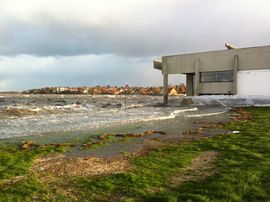 Bølgerne slår ind over molen og græsset ved Vikingeskibshallen.