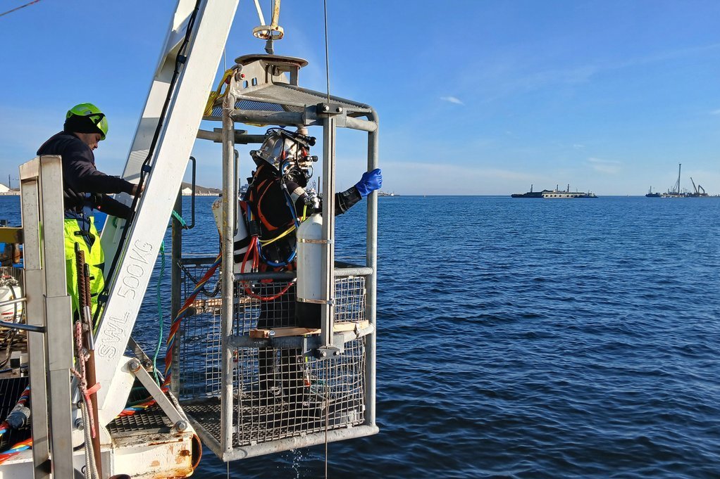 Vikingeskibsmuseets arkæologer arbejder fra en stor dykker platform. Her ses en marinarkæolog i dykkerelevatoren på vej ned til udgravning i 15 meters dybde.