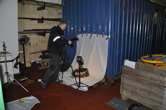 Op ad en container i øverste lastrum har vi opstillet et midlertidigt fotostudie, hvor genstandene fotograferes efterhånden som de bjærges. Her fotograferer Morten Johansen, Vikingeskibsmuseet den bevarede kant af kobberkarret. Foto: David Gregory