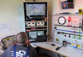 Dykkerne på bunden ledes af dykkerlederen fra en container på dykkerflådens dæk. Her følges arbejdet på skærme og dykkerne instrueres af dykkerlederen via dykkertelefonen. På panelet til højre aflæses og justeres luftblanding, lufttryk, dybde mv Dykkerne på bunden ledes af dykkerlederen fra en container på dykkerflådens dæk. Her følges arbejdet på skærme og dykkerne instrueres af dykkerlederen via dykkertelefonen. På panelet til højre aflæses og justeres luftblanding, lufttryk, dybde mv