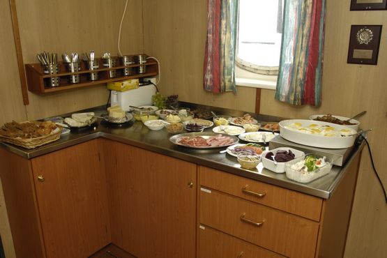 I messen er der rettet an til frokost. Om bord på VINA spiser man godt. Frokostbuffeten består af et udvalg af sild, pålæg, gode oste og en varm ret – her hakkebøf med spejlæg. Foto: Morten Johansen, Vikingeskibsmuseet. I messen er der rettet an til frokost. Om bord på VINA spiser man godt. Frokostbuffeten består af et udvalg af sild, pålæg, gode oste og en varm ret – her hakkebøf med spejlæg. Foto: Morten Johansen, Vikingeskibsmuseet.